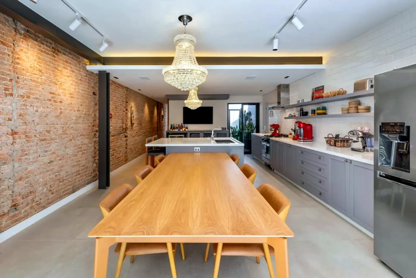 Cozinha e sala de jantar integradas, com mesa longa de madeira e parede de tijolinho aparente