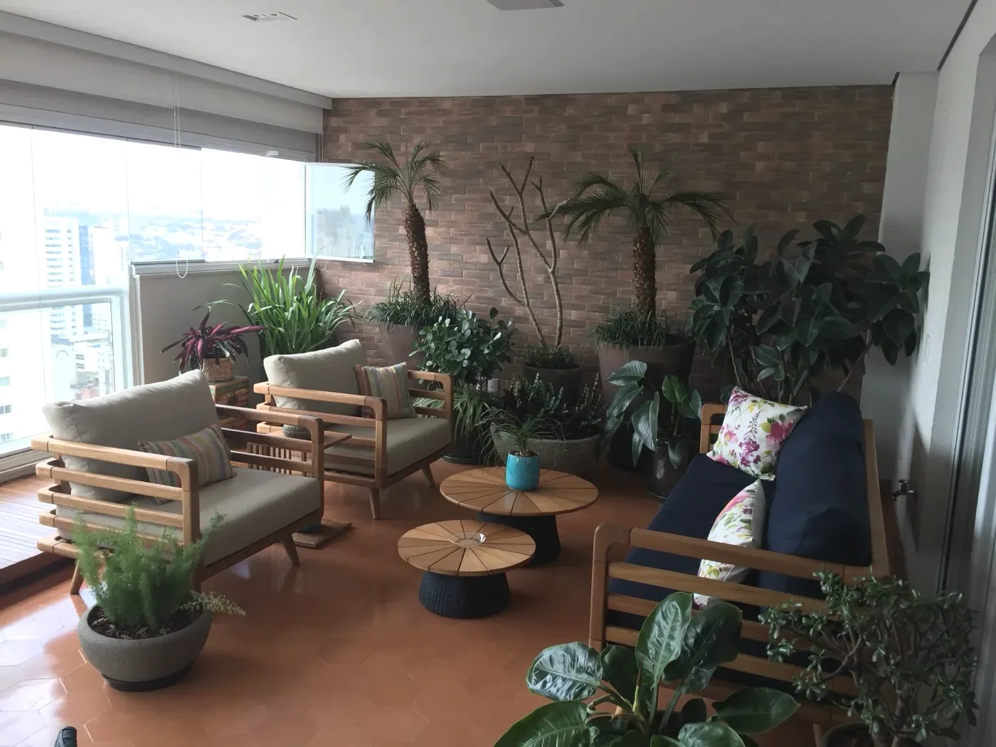 Varanda ampliada com jardim, poltronas de madeira e parede de tijolinho aparente