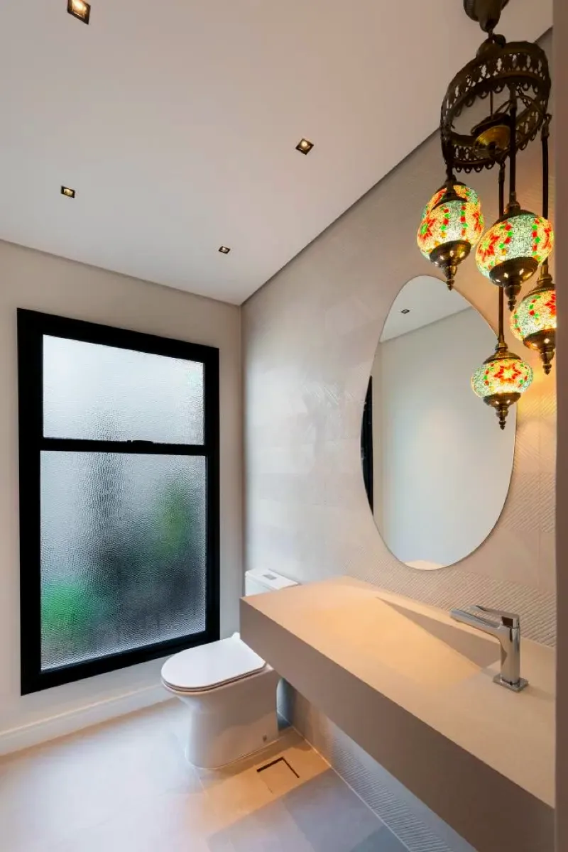 Lavabo com bancada suspensa, espelho oval e luminárias decorativas